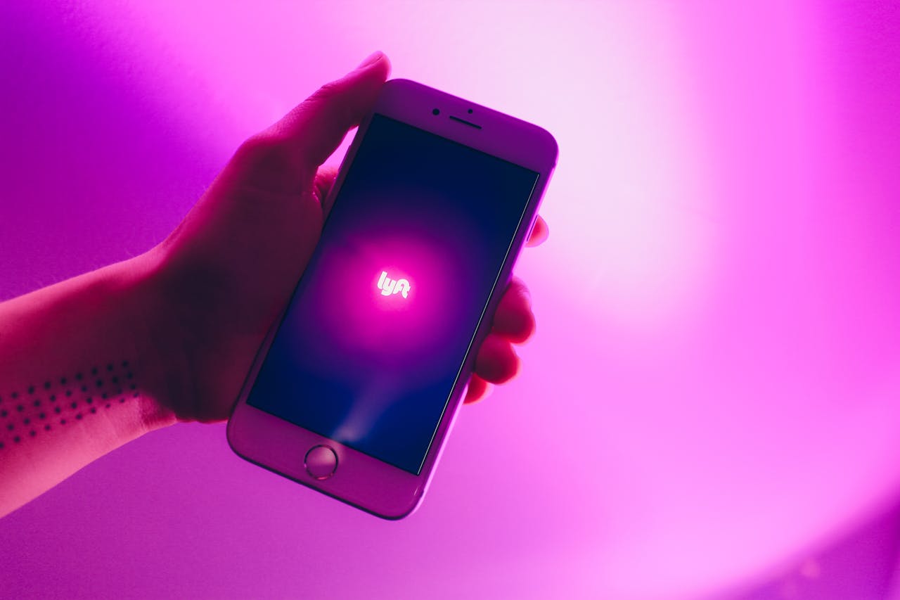 home-hero A hand holding a smartphone displaying the Lyft ridesharing app with a vivid pink background.