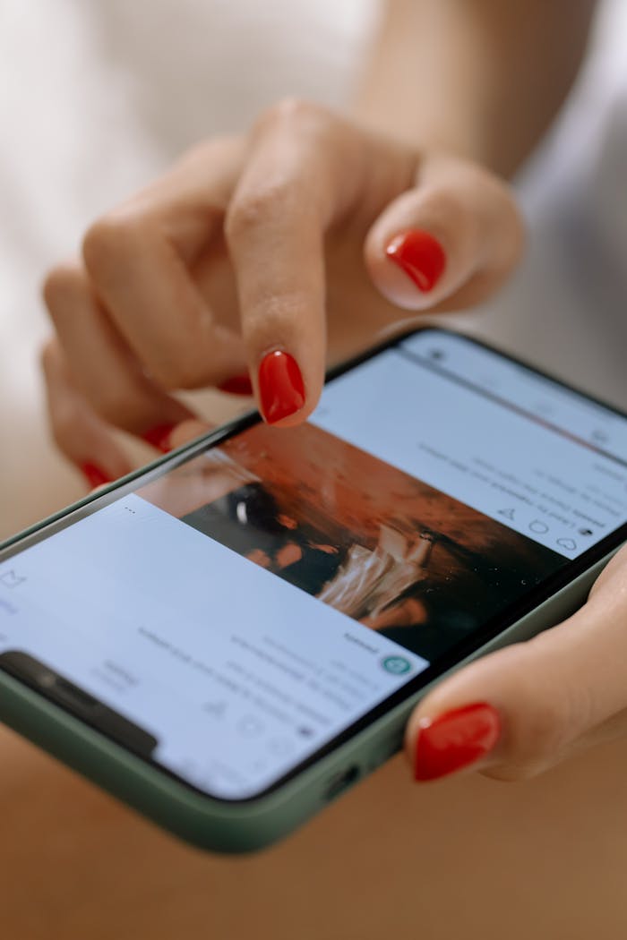 services-06 A woman with red nails using a smartphone, navigating a social media app.
